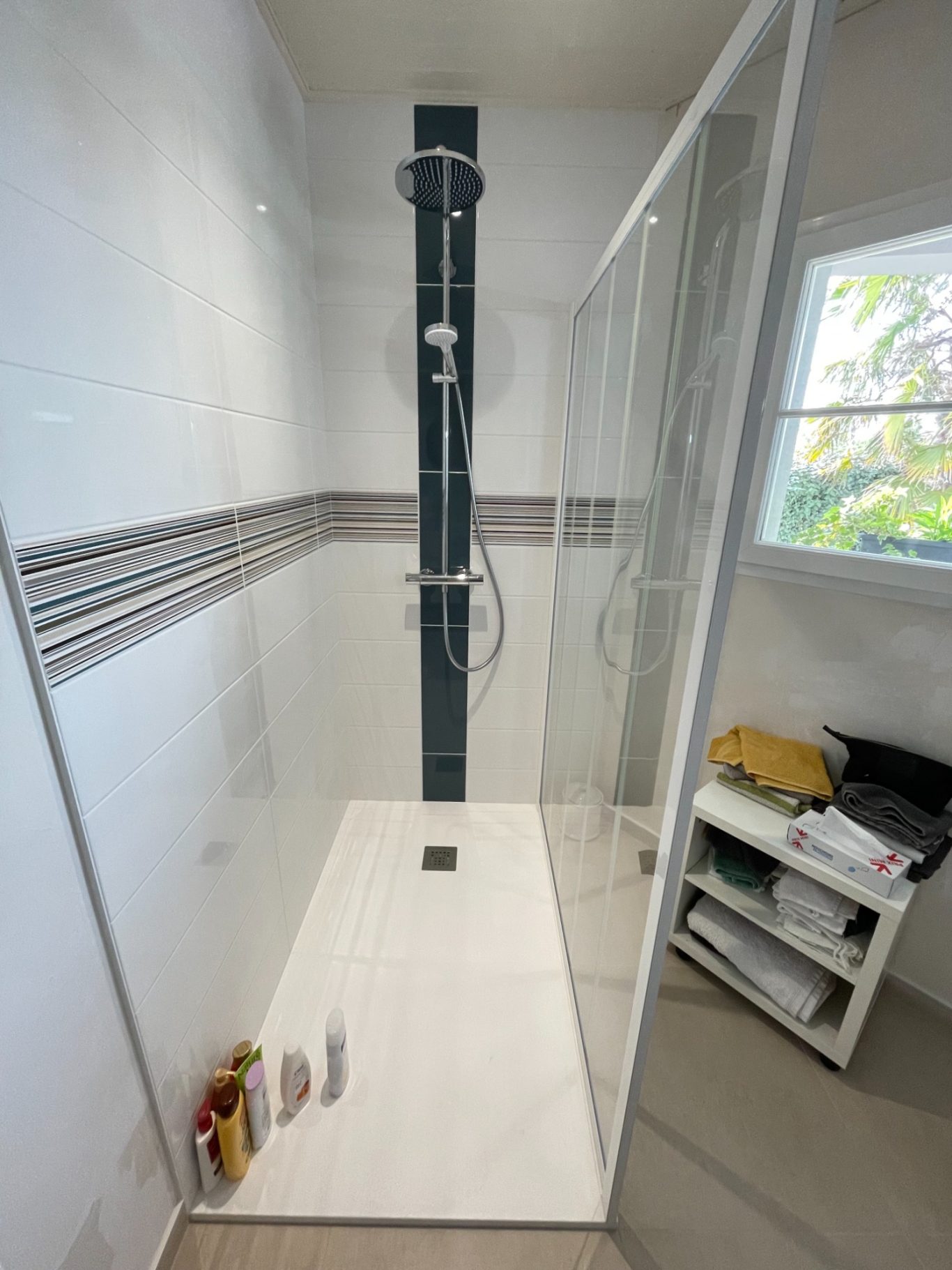 Douche moderne avec parois en verre, carrelage blanc et colonne de douche noire.