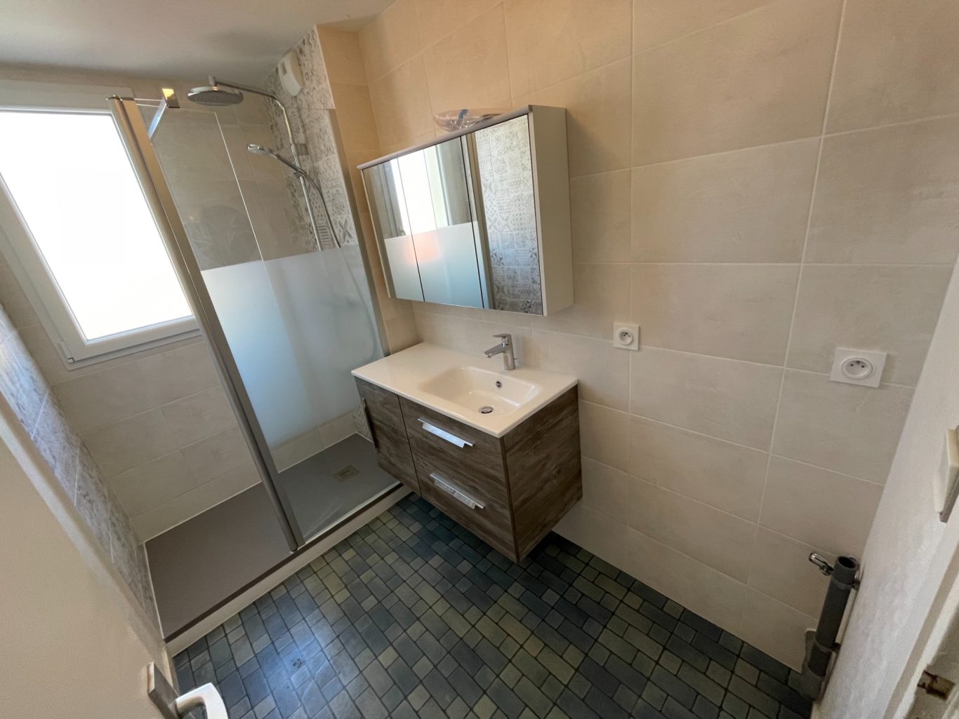 Salle de bain moderne avec douche, lavabo sur meuble en bois et carrelage vert.