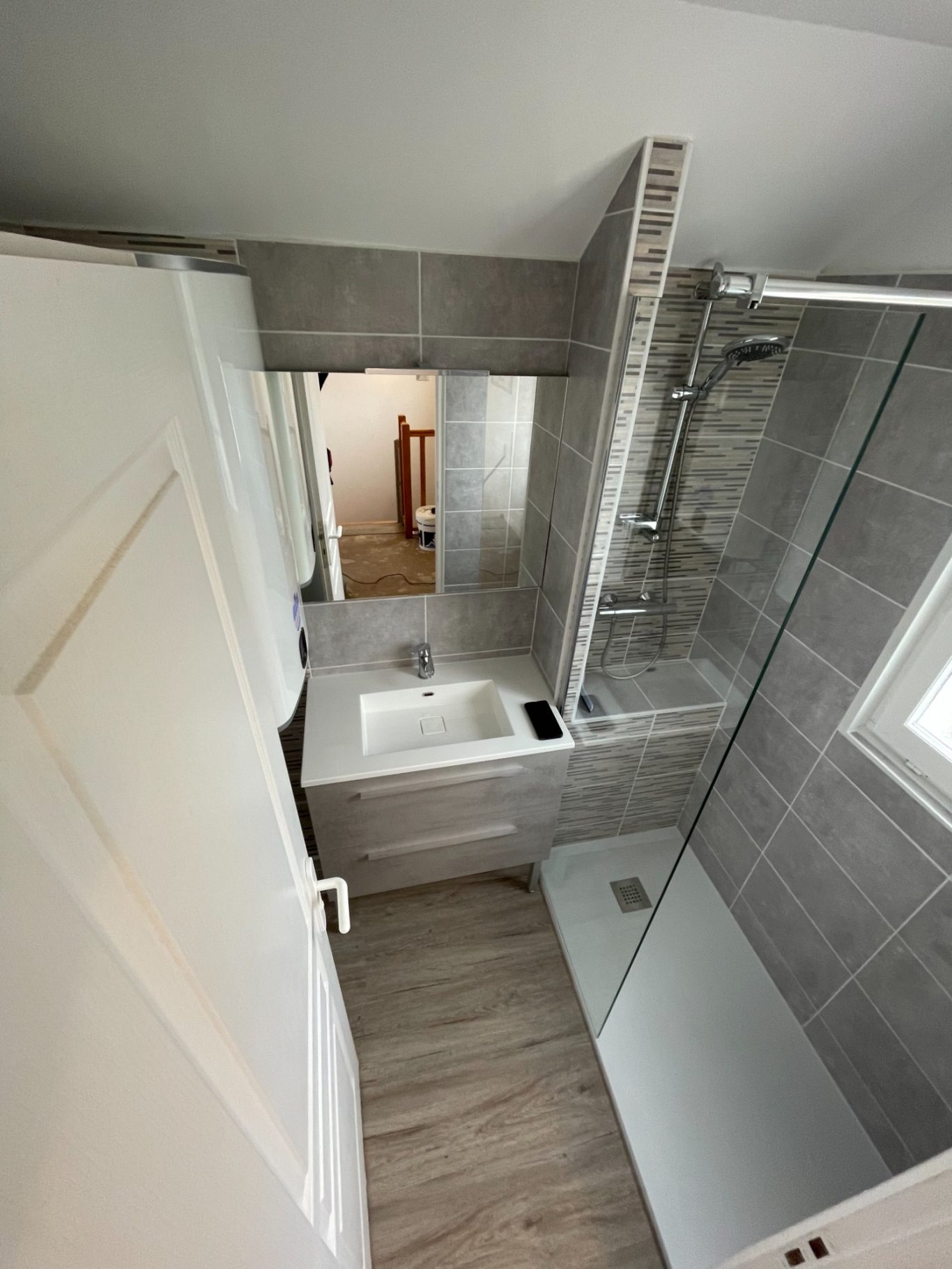 Salle de bain moderne avec douche, lavabo et miroir, revêtement en carrelage clair.