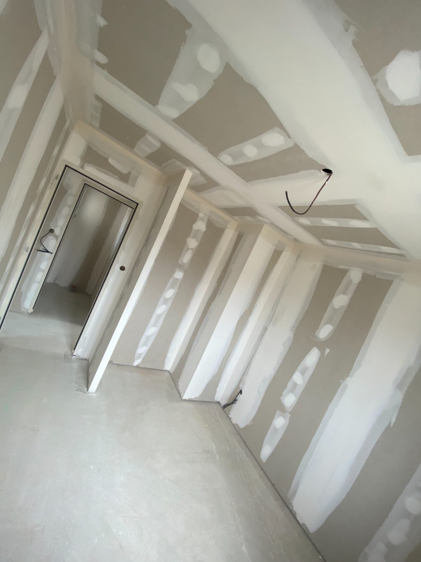 Pièce vide avec murs en plaques de plâtre non peints et sol en béton clair.