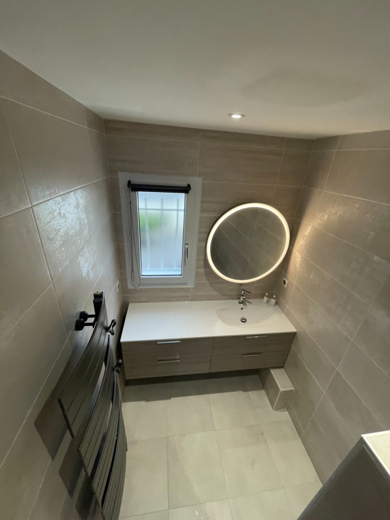 Salle de bain moderne avec miroir rond et meuble sous lavabo.
