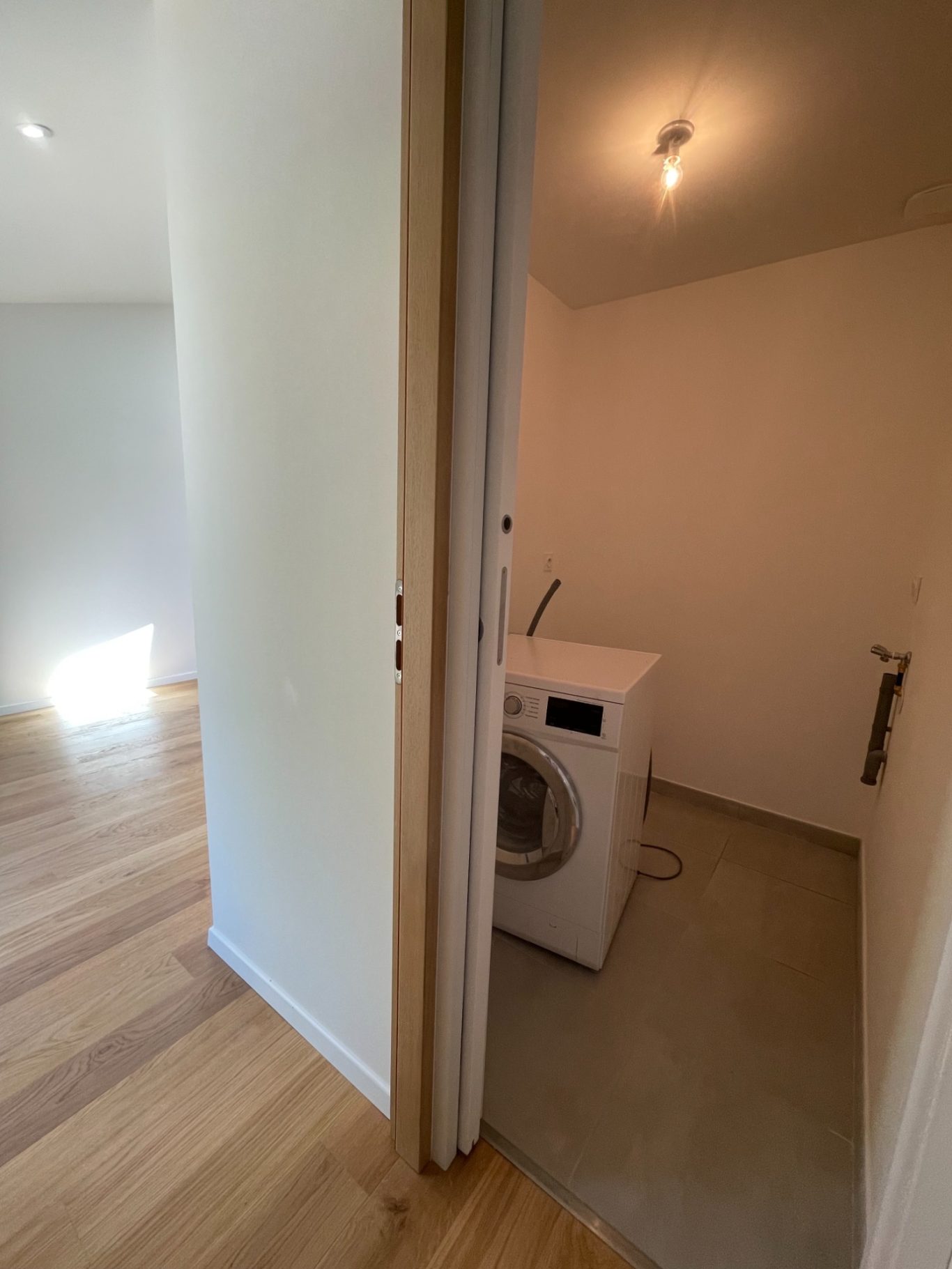 Une buanderie avec un lave-linge dans une pièce claire aux murs blancs.