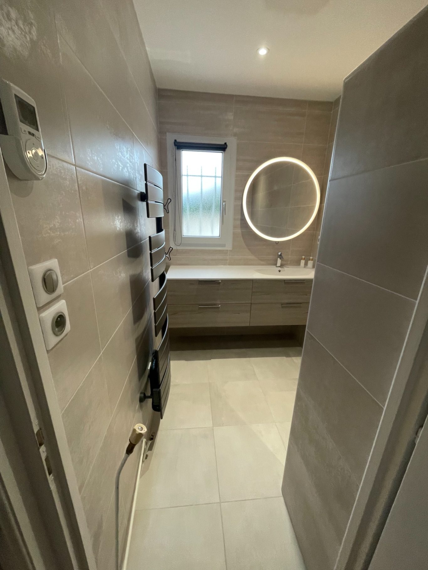 Salle de bains moderne avec un miroir rond et des murs en carrelage gris.