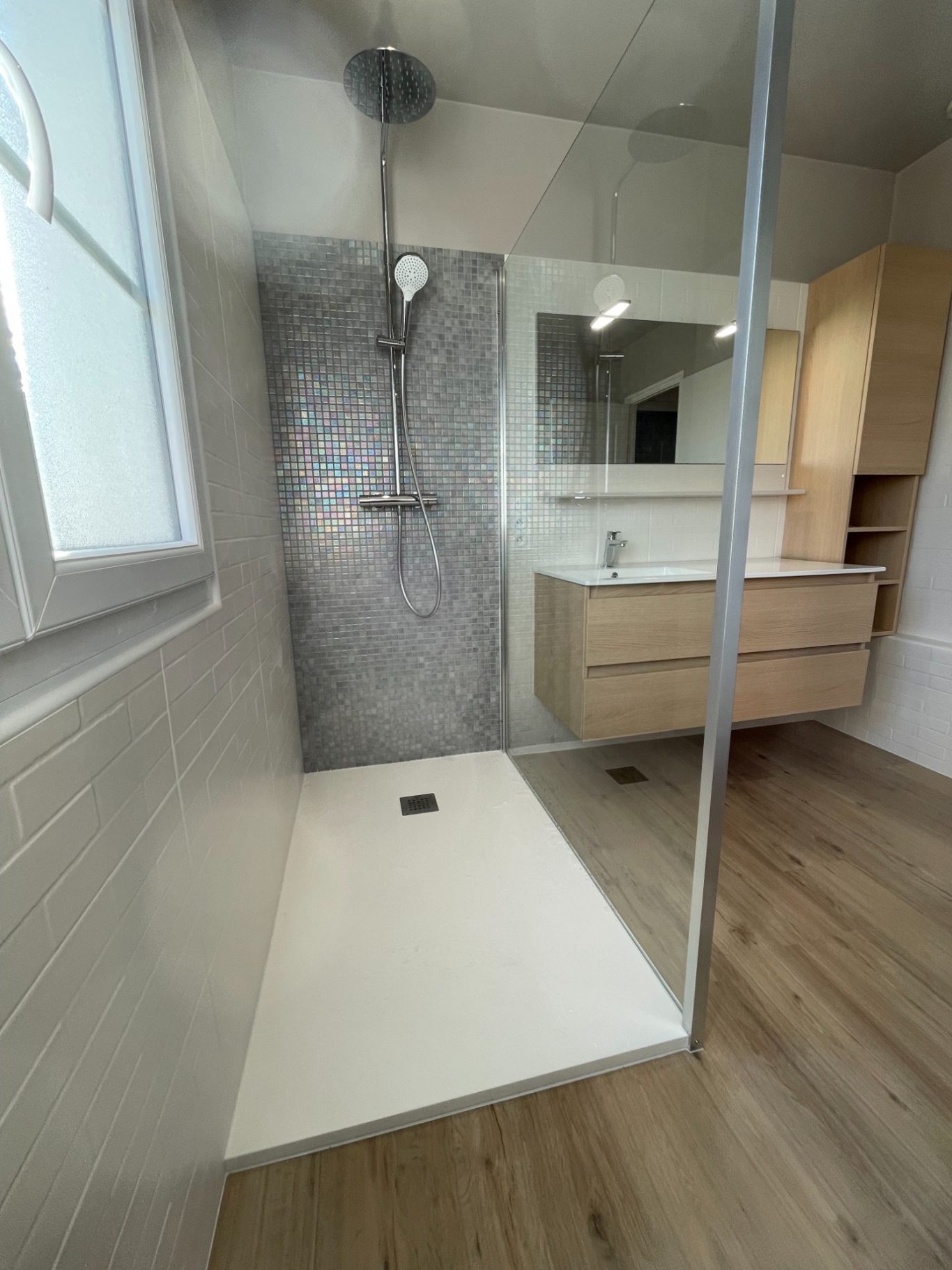 Salle de bains moderne avec douche, meuble en bois et carrelage gris.