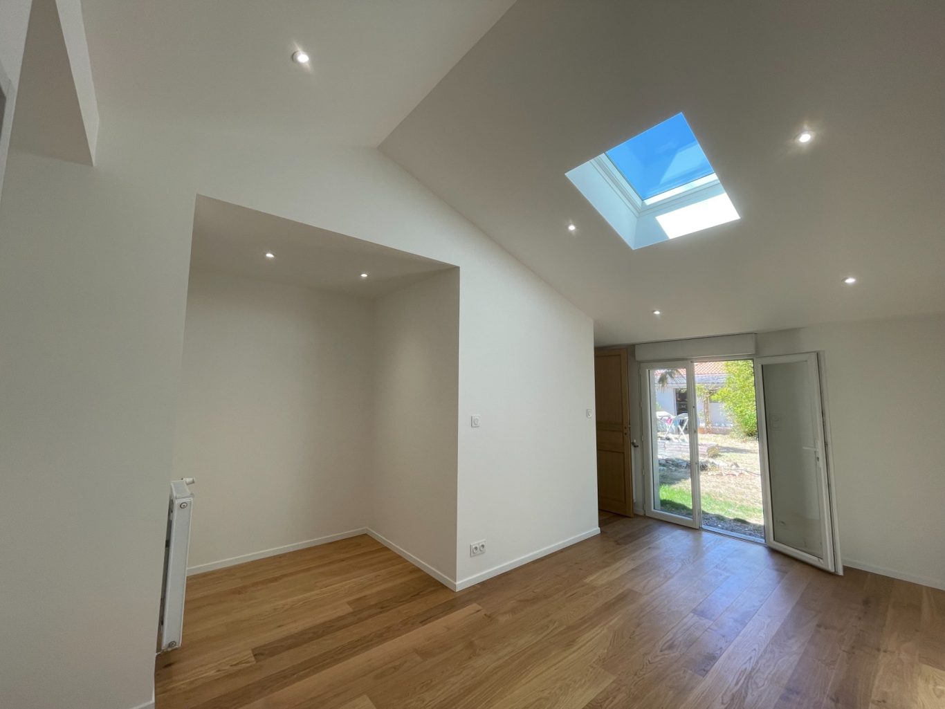 Intérieur d'une pièce lumineuse avec un toit en pente et des fenêtres. Sol en bois.