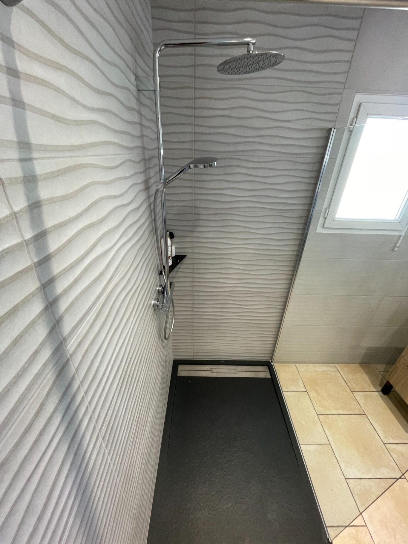 Douche moderne avec parois texturées et sol noir, fenêtre au-dessus.