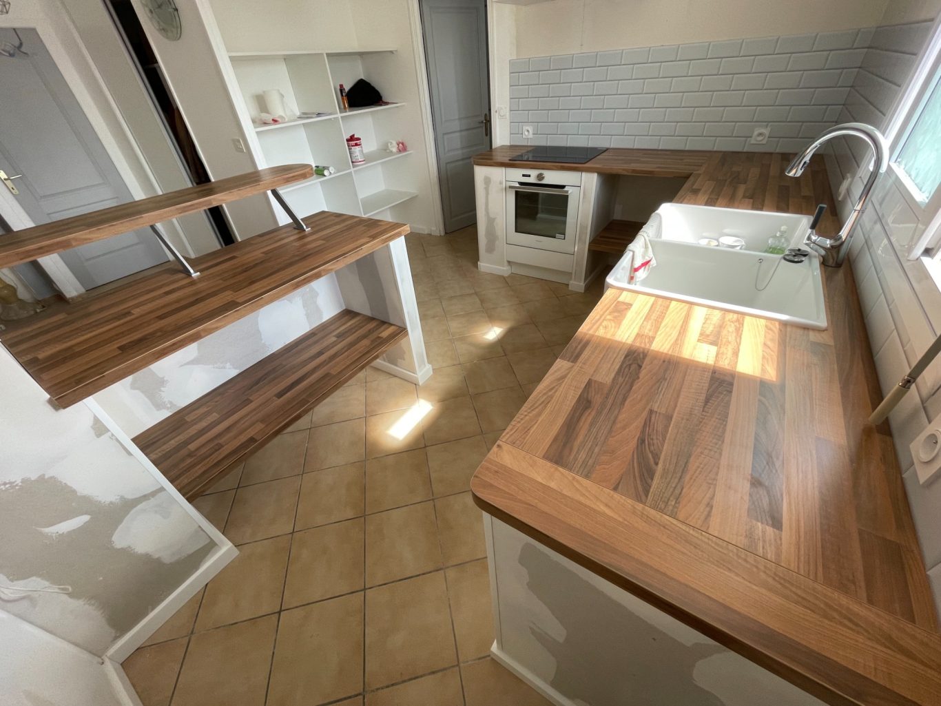 Cuisine moderne avec plan de travail en bois et étagères ouvertes, carrelage clair.