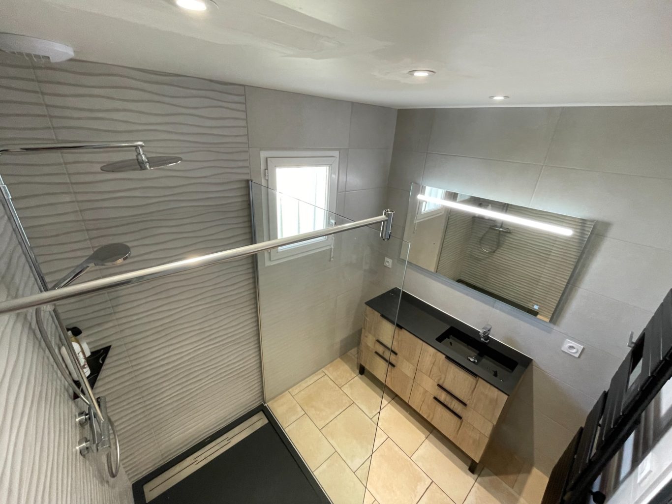 Salle de bain moderne avec douche, miroir et meuble en bois.