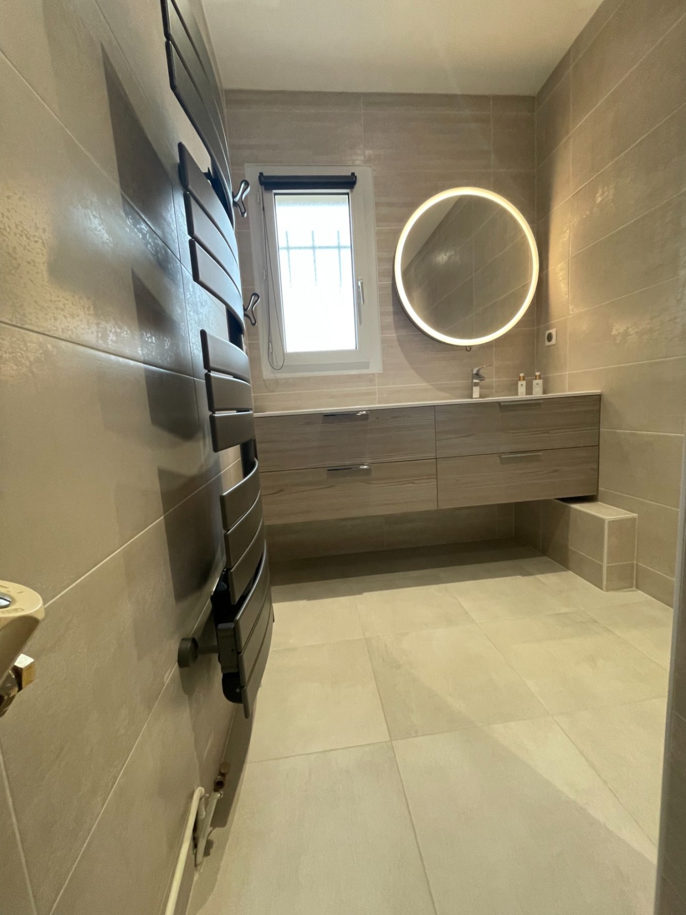 Salle de bain moderne avec sols en carrelage, miroir rond et meuble sous-lavabo.