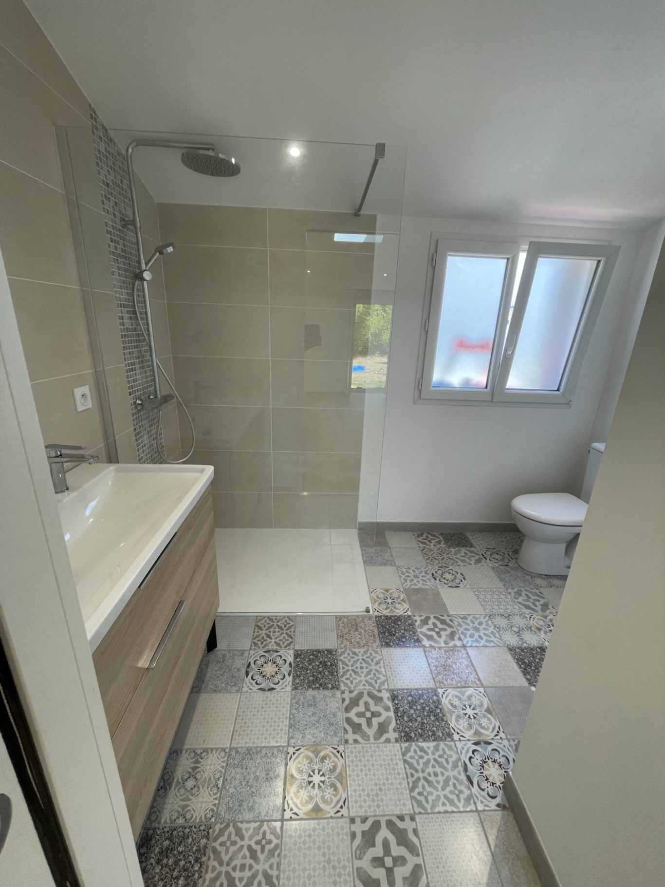 Salle de bain moderne avec douche, lavabo et toilettes, carrelage décoratif au sol.