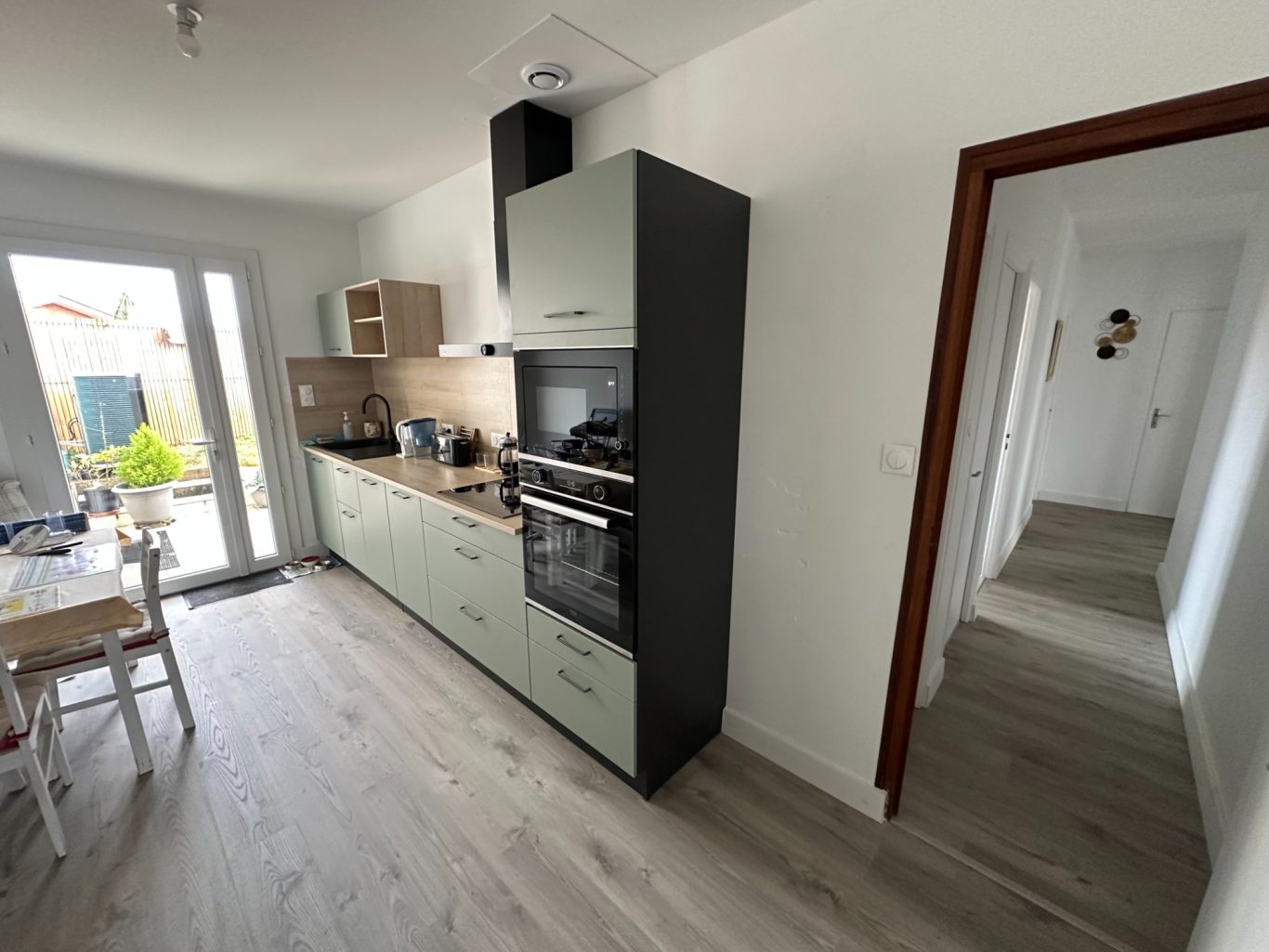 Cuisine moderne avec meubles vert clair, appareil en inox, et accès à l'extérieur.