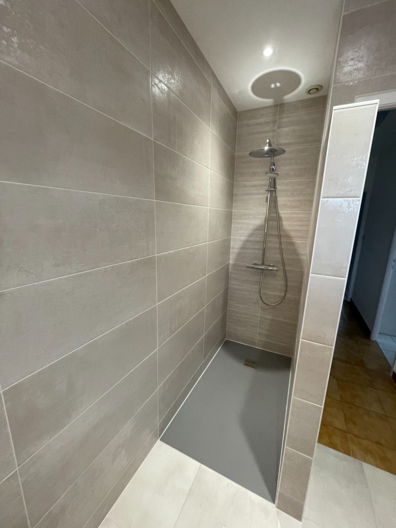 Douche moderne avec carrelage gris et robinet au plafond. Sol en résine grise.