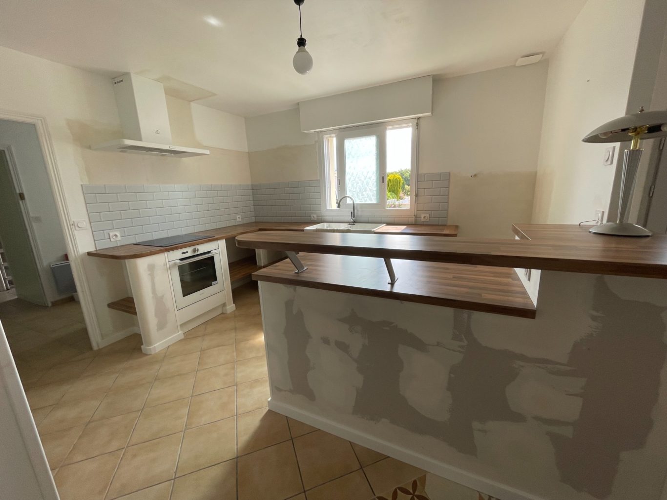 Cuisine moderne avec un comptoir en bois, réfrigérateur et fenêtres lumineuses.