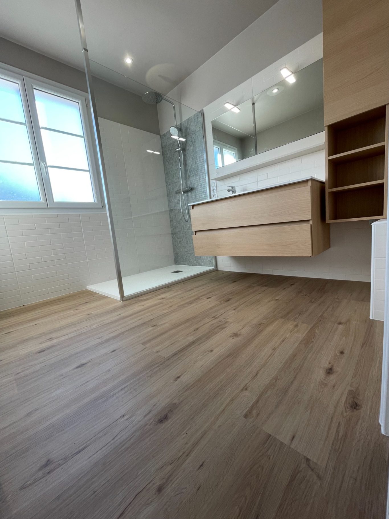 Salle de bains moderne avec douche, meuble suspendu et sol en bois clair.